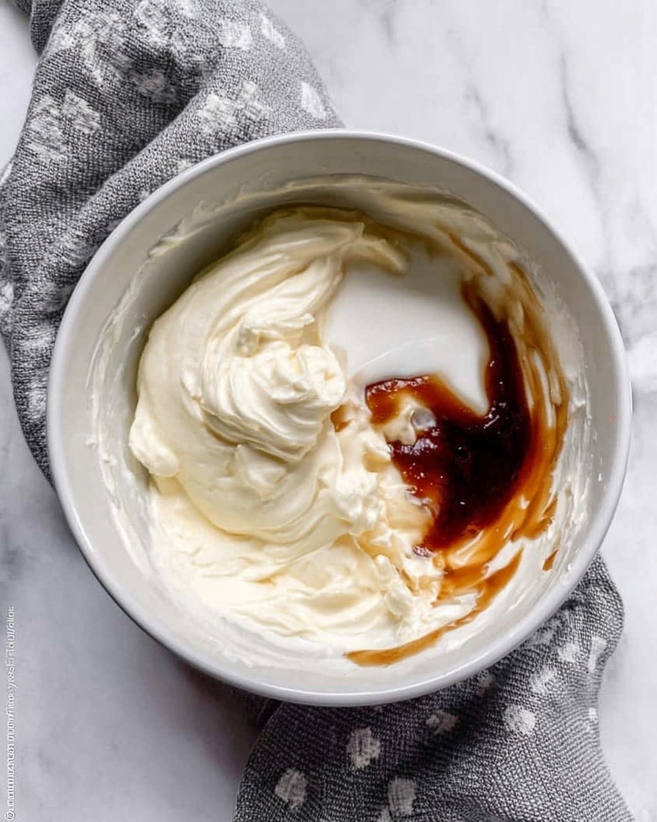 A white bowl filled with three different ingredients: creamy white and thick mixture covering most of the bowl, a smaller amount of smooth white cream, and a dark brown syrupy liquid poured on top near the side. A woman's hand is not visible, but a grey cloth with white patterns lays beside the bowl on a white marbled surface. photo taken with an iphone --ar 4:5 --v 7