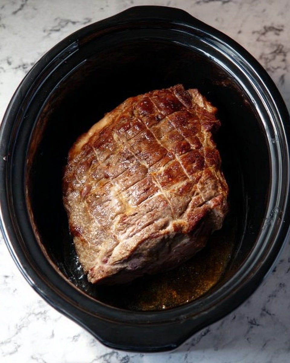 A large piece of cooked meat with a brown, slightly crispy surface sits in the center of a black slow cooker pot. The meat shows grill marks and some visible texture from cooking. The background is a white marbled surface. photo taken with an iphone --ar 4:5 --v 7