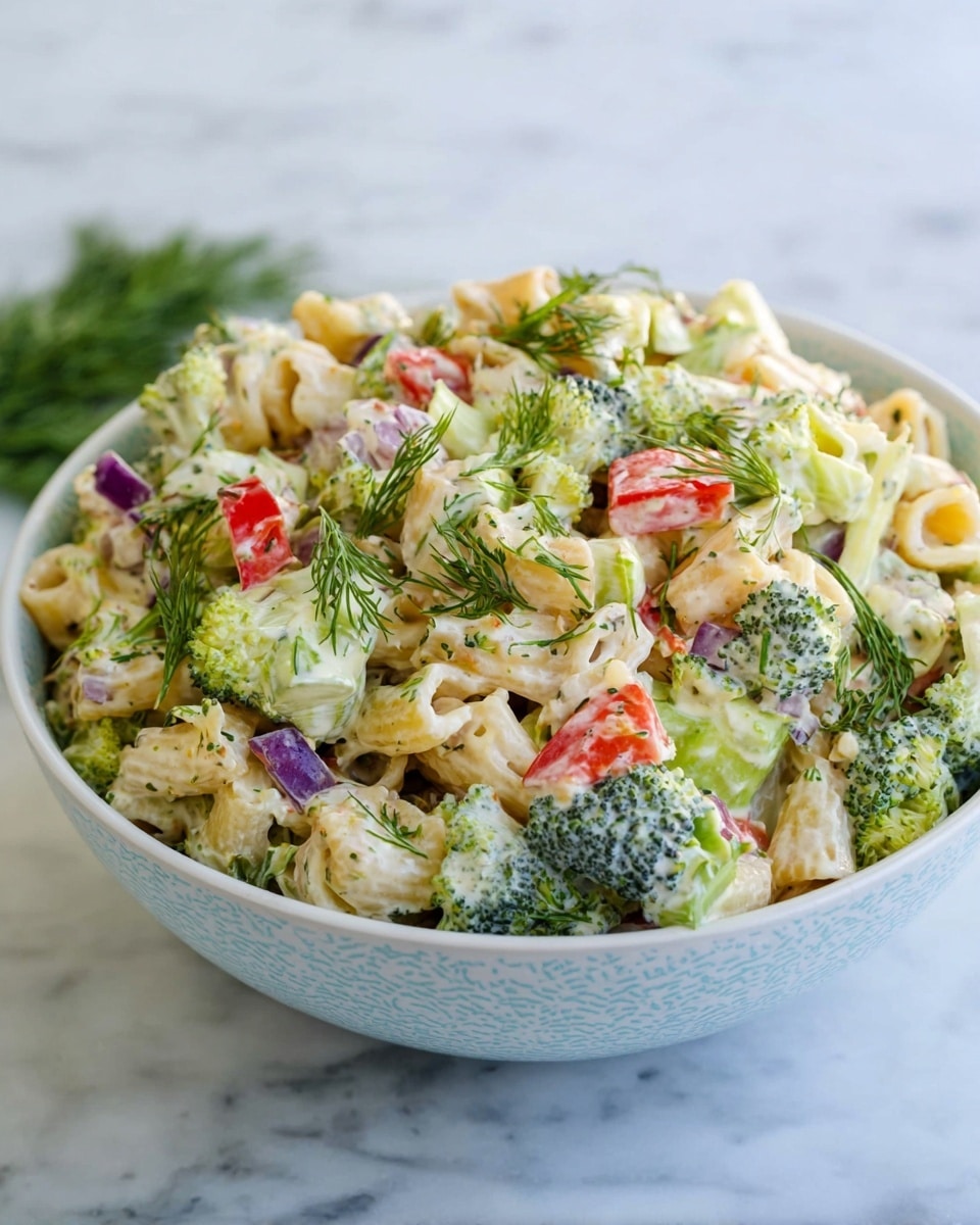 A bowl of pasta salad sits on a white marbled surface. The bowl is white with a soft blue pattern and filled with small, tube-shaped pasta mixed with creamy dressing. The salad has layers of green broccoli florets, pale green lettuce pieces, bits of purple onion, and bright red bell pepper chunks scattered on top. Fresh dill sprigs add touches of green throughout. The textures vary from smooth creamy pasta to crisp fresh vegetables. Photo taken with an iphone --ar 4:5 --v 7