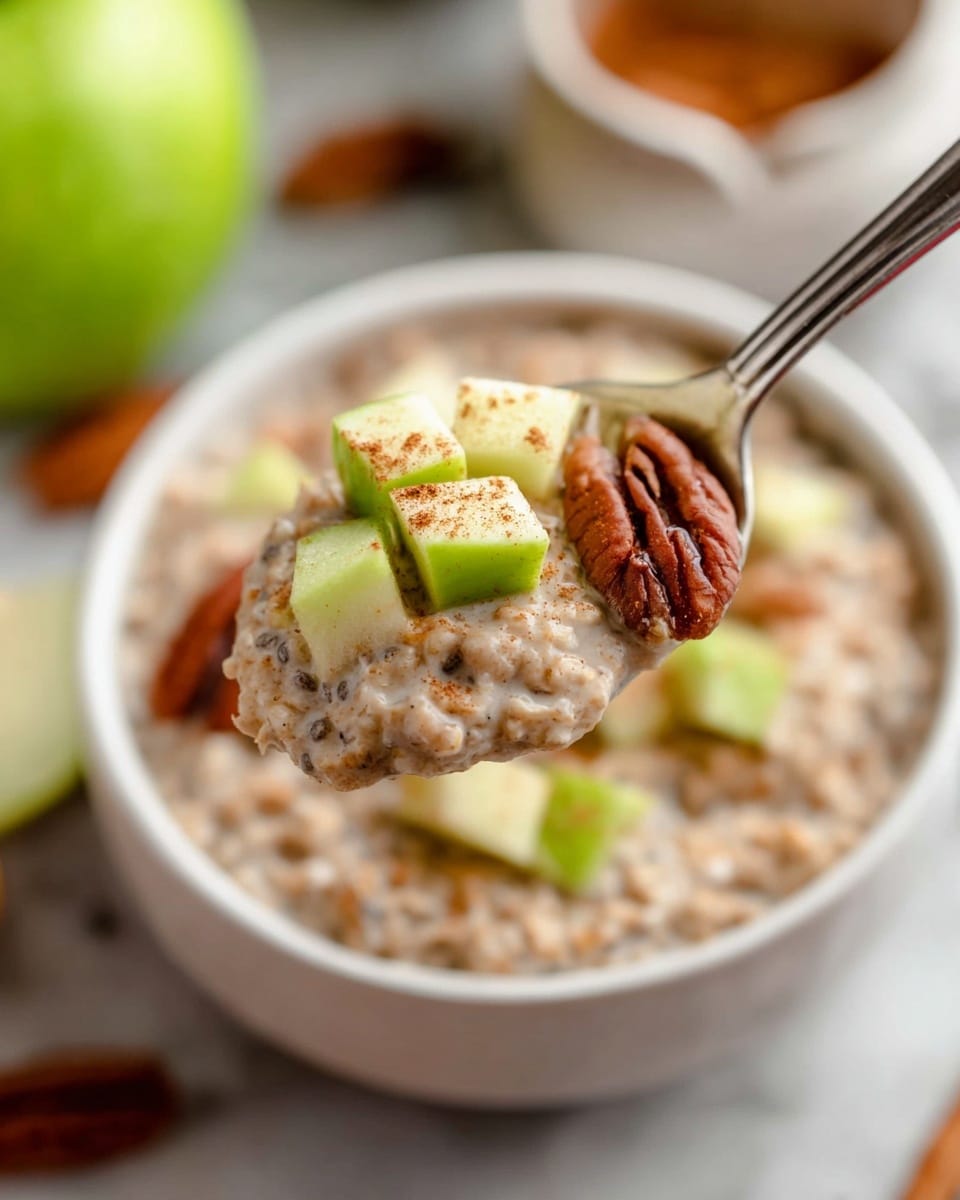 A close-up of a spoon holding thick oatmeal with visible chia seeds, topped with small bright green apple cubes dusted lightly with cinnamon and a few glossy brown pecans. The spoon is held over a white bowl filled with the same oatmeal mixture and garnished with more green apple pieces and pecans. The background shows a white marbled surface with a blurry half green apple and a bowl of oats. The colors are warm and natural, with soft lighting highlighting the creamy texture of the oatmeal and the fresh, crisp look of the apple pieces. photo taken with an iphone --ar 4:5 --v 7
