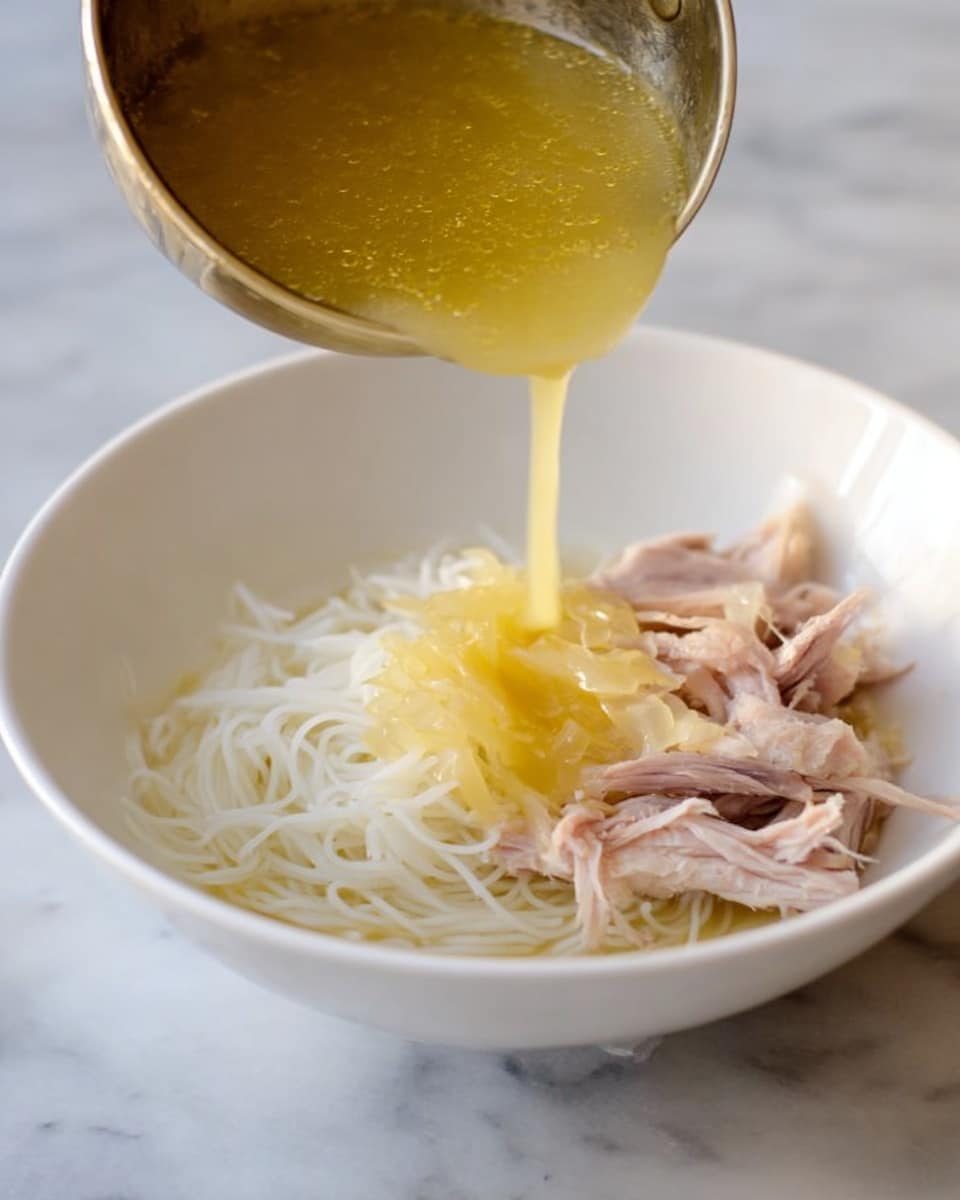 A white bowl on a white marbled surface holds thin white noodles on the right side and thin slices of light pink cooked meat underneath and to the left. Yellow broth mixed with cooked translucent onions is being poured into the bowl from a silver ladle held by a woman's hand above the bowl. The broth has a smooth texture and is mid-pour, pooling on top of the noodles and meat. Photo taken with an iphone --ar 4:5 --v 7