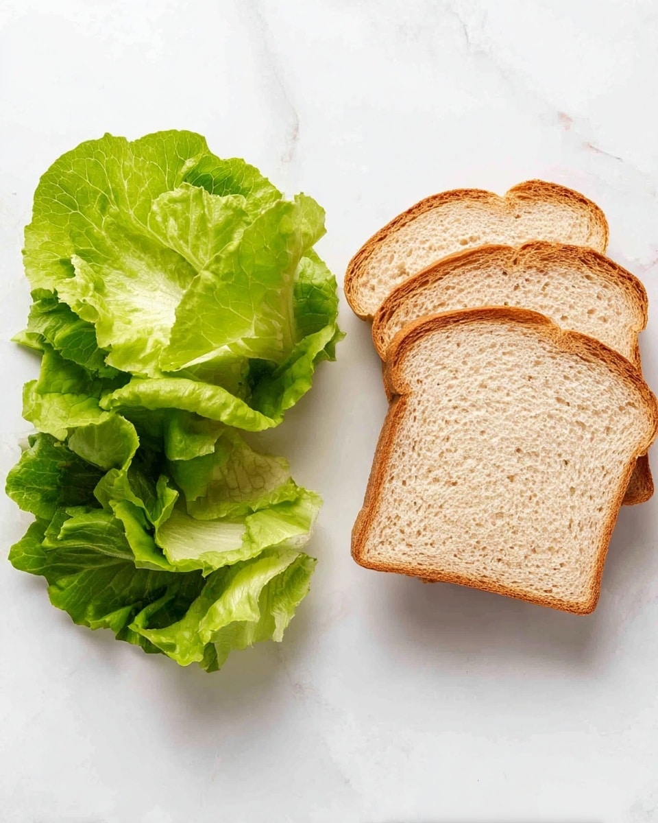 The image shows two groups of items side by side on a white marbled surface. On the left, there is a small stack of bright green lettuce leaves with soft, ruffled edges and a fresh texture. On the right, there are three slices of light brown bread with a soft, slight texture and thin crusts placed in a small pile overlapping slightly. photo taken with an iphone --ar 4:5 --v 7