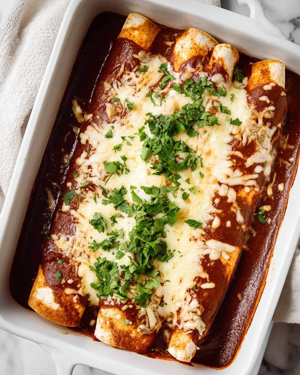 The image shows a white rectangular baking dish filled with five rolled enchiladas. The enchiladas are covered with a rich, reddish-brown sauce, mostly covering the middle and sides. A layer of melted creamy white cheese is spread evenly over the top, with some spots thicker than others. Bright green chopped fresh cilantro is sprinkled over the cheese, mainly in the center and a little to the right. The baking dish sits on a white marbled surface with a white cloth nearby. photo taken with an iphone --ar 4:5 --v 7