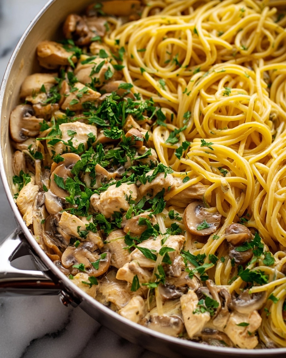 The image shows a close-up of a white pan filled with a creamy pasta dish. The first layer has yellow spaghetti noodles mixed evenly with small pieces of light brown chicken and sliced beige mushrooms. The top layer is sprinkled with fresh green parsley, adding a bright color contrast. The noodles have a smooth, shiny texture, and the chicken pieces look soft and tender. The pan rests on a white marbled surface, and the background is softly blurred. photo taken with an iphone --ar 4:5 --v 7