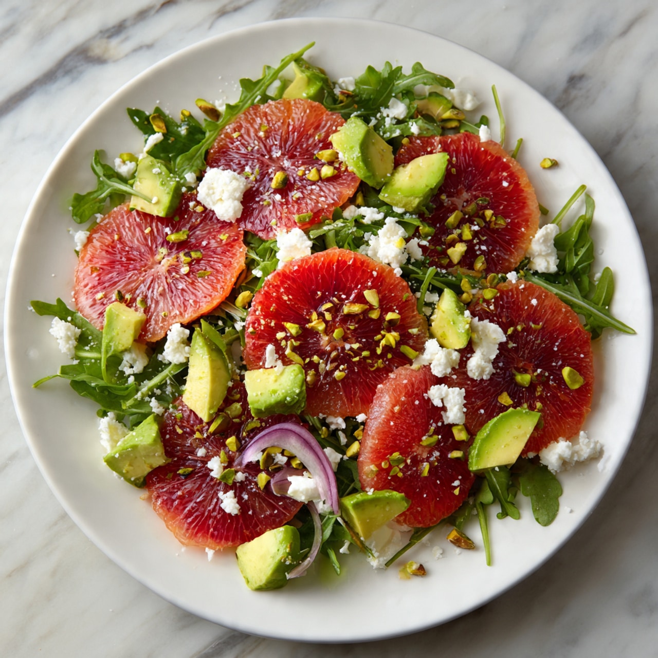 The dish shows a white plate filled with green leafy arugula as the base layer, topped with several bright red blood orange slices placed evenly across the salad. Light green avocado chunks are scattered among the orange slices, adding a creamy texture. Small crumbles of white cheese are spread throughout, along with thin slices of purple-red onion rings. The salad is finished with sprinkled light brown chopped pistachios, adding a crunchy detail. The plate sits on a white marbled surface. photo taken with an iphone --ar 4:5 --v 7