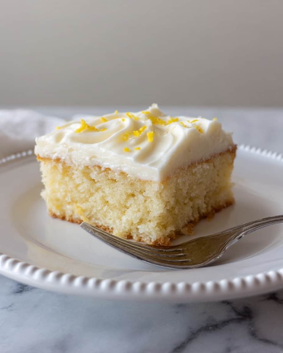A single small square piece of cake sits on a white plate with a beaded edge. The cake has two layers: the bottom layer is a light golden sponge with a soft, crumbly texture, and the top layer is a thick spread of white creamy frosting that is slightly wavy with small yellow sprinkles on top. A silver fork rests next to the cake on the plate. The background features a white marbled surface and soft, neutral walls. photo taken with an iphone --ar 4:5 --v 7