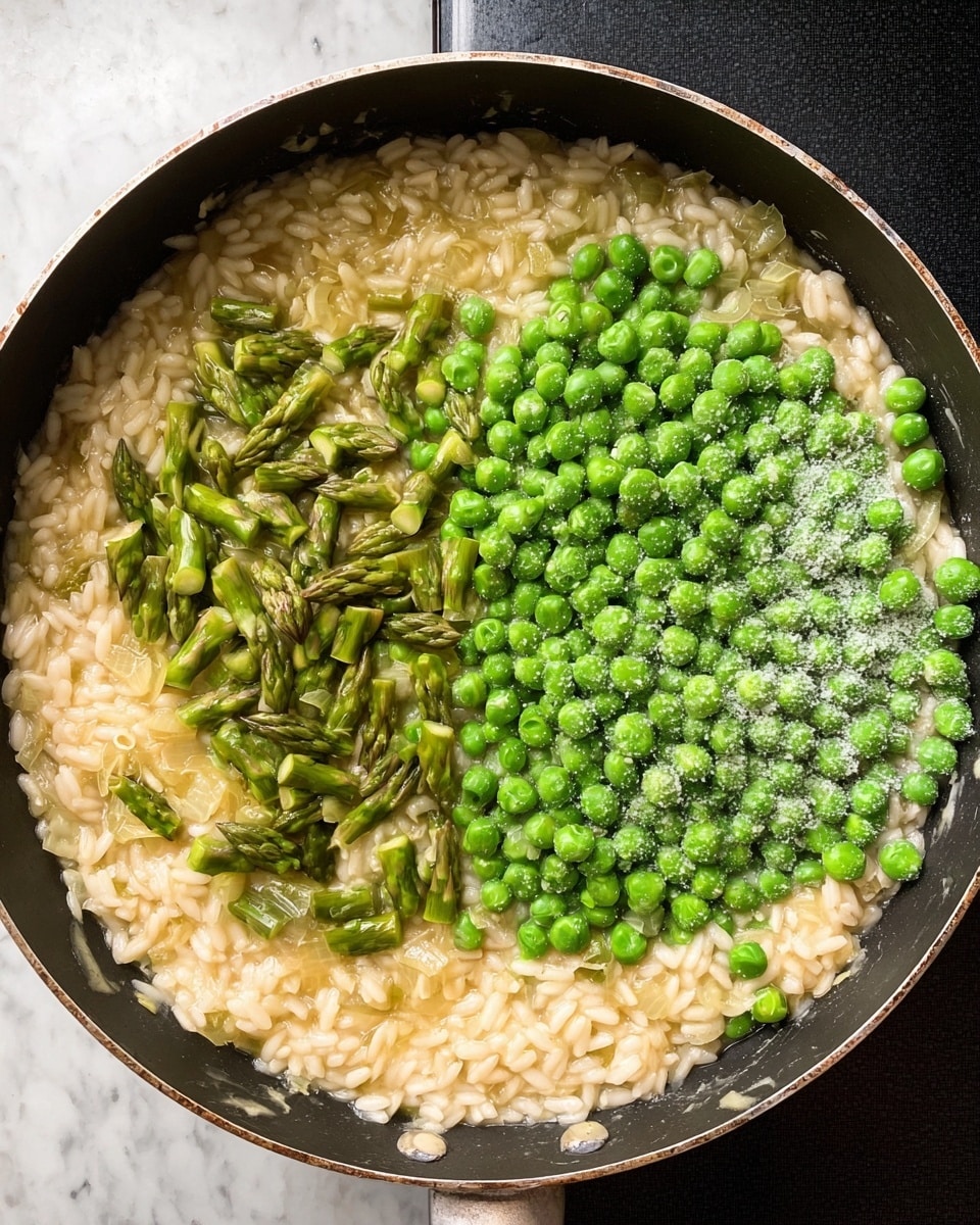 A top view of a large black pan filled with creamy risotto rice that is pale yellow and soft, mixed with small pieces of cooked onion. On top of the risotto, there are two sections: on the left, bright green chopped asparagus pieces with a fresh texture; on the right, a pile of vibrant green frozen peas covered with a light frost. The pan sits on a black induction stove, and the background is a white marbled surface. photo taken with an iphone --ar 4:5 --v 7