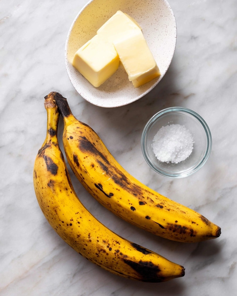 Two ripe yellow plantains with black spots lie side by side on a white marbled surface. Above them, there is a white bowl with small black speckles containing two thick slices of pale yellow butter, and next to it is a small clear glass bowl holding a bit of coarse white salt. The scene is simple with a focus on these few ingredients, with soft natural light and shadows visible. photo taken with an iphone --ar 4:5 --v 7
