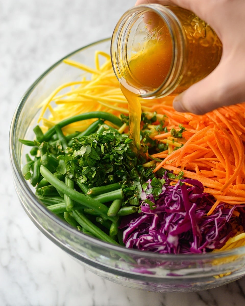 A clear glass bowl sits on a white marbled surface filled with five distinct layers of fresh vegetables arranged in segments: green beans in the bottom left, thin yellow strips on the bottom right, finely chopped green herbs above the green beans, grated orange carrots piled in the top right, and shredded purple cabbage in the top left. A woman's hand is seen pouring golden-brown dressing from a small clear glass jar onto the vegetables, with a close-up focus on the pouring action. Photo taken with an iphone --ar 4:5 --v 7