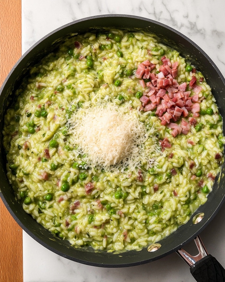 A black pan filled with a creamy green risotto showing visible grains of rice and green peas mixed throughout. In the center, there is a small mound of finely grated white cheese. To the right of the cheese, there is a small pile of pink diced cooked bacon pieces resting on the risotto. The pan is placed on a white marbled surface. photo taken with an iphone --ar 4:5 --v 7