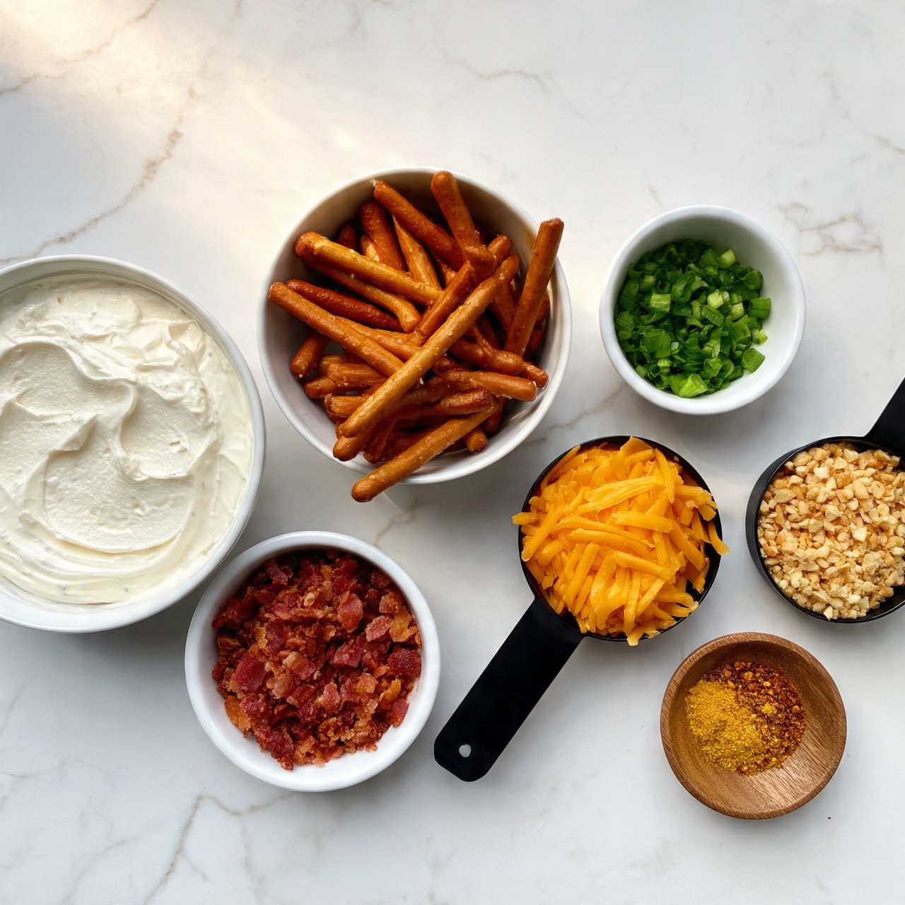 The image shows eight small bowls and measuring cups arranged on a white marbled surface, each containing different food ingredients. The largest bowl on the left holds a creamy white mixture with a smooth texture. Next to it is a medium white bowl filled with brown pretzel sticks lying flat. Below this is a smaller white bowl filled with crispy reddish-brown bacon bits. A black measuring cup is filled with orange-yellow shredded cheddar cheese, placed slightly to the right and in front of the pretzels. To its right is another black measuring cup containing finely chopped light brown nuts. Above it is a small white bowl with finely chopped bright green onions. On the far right, a small wooden bowl holds a mix of yellow and reddish spices. All items are neatly spaced on a white marbled surface, with soft natural light highlighting their colors and textures. photo taken with an iphone --ar 4:5 --v 7